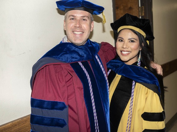 A male professor and a female professor dressed in graduation regalia backstage in Centennial Hall.