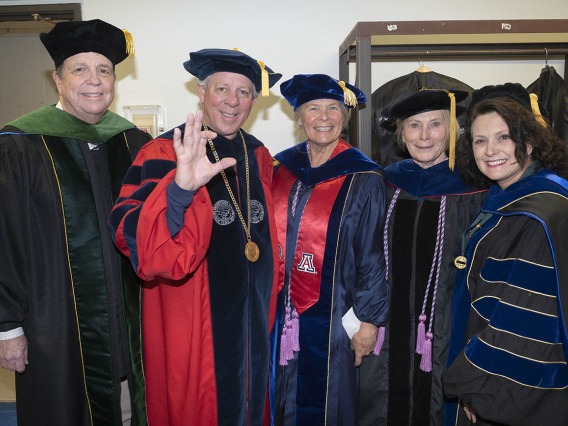 Five university leadership and faculty members dressed in graduation regalia smile before taking the stage in Centennial Hall.