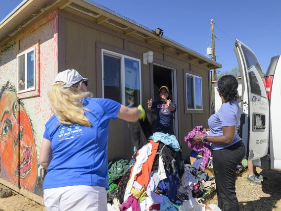 Three women sorting a big pile of donated clothing outside of a small building. 