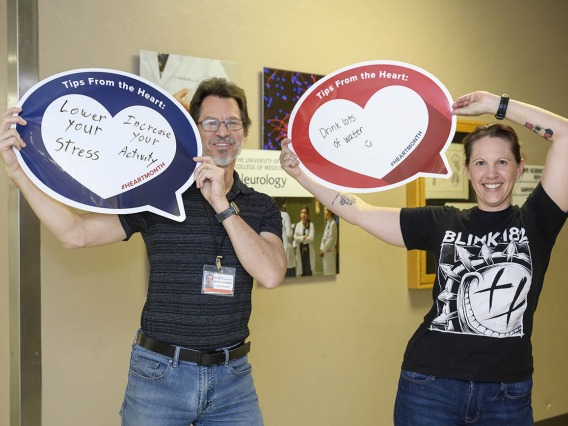 Man and woman in dark shirts hold up heart posters