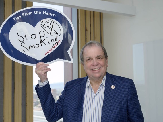 Older white man in blue sport coat holds up sign that says Stop Smoking!