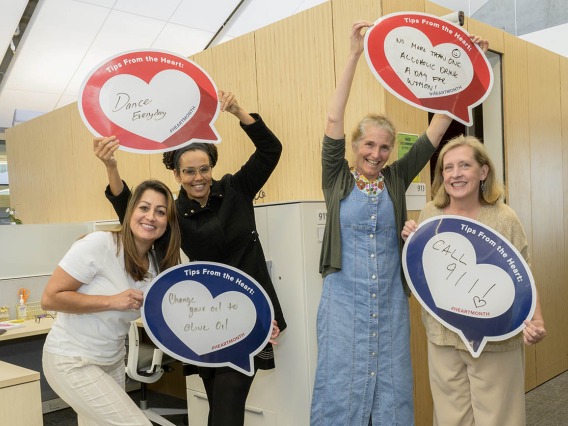 4 woman stand in an office holding heart posters. 