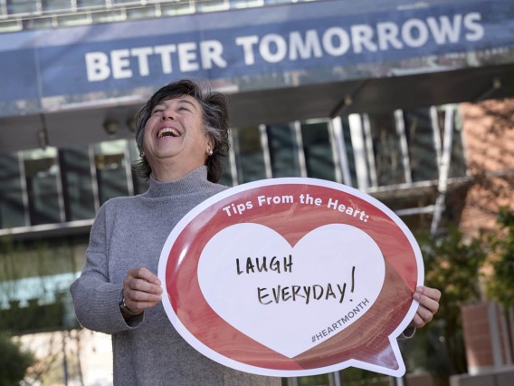 Middle-aged woman with short dark hair laughs as she holds a heart poster that says Laugh everyday!