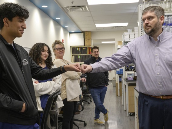 Esteban Ramirez, a student from Pima County JTED, a technical education program for high school students, bumps fists with Nathan Cherrington, PhD (right), director of the Southwest Environmental Health Sciences Center, at a January tour of his lab in the R. Ken Coit College of Pharmacy. 