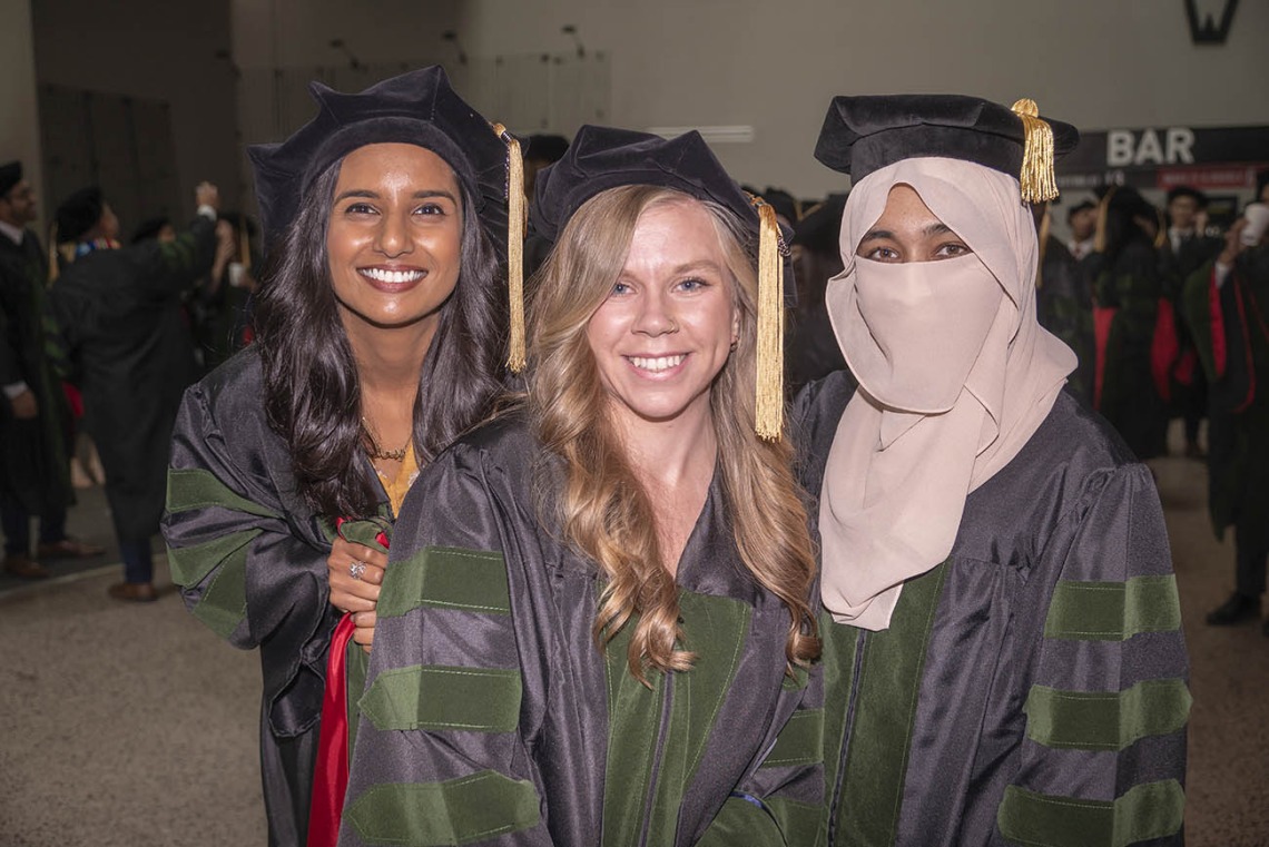 Three young women wearch graduation caps and gowns smile.
