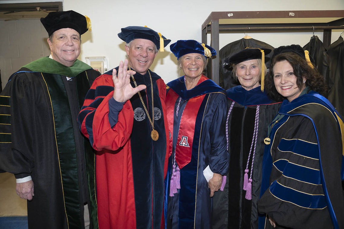 Five university leadership and faculty members dressed in graduation regalia smile before taking the stage in Centennial Hall.