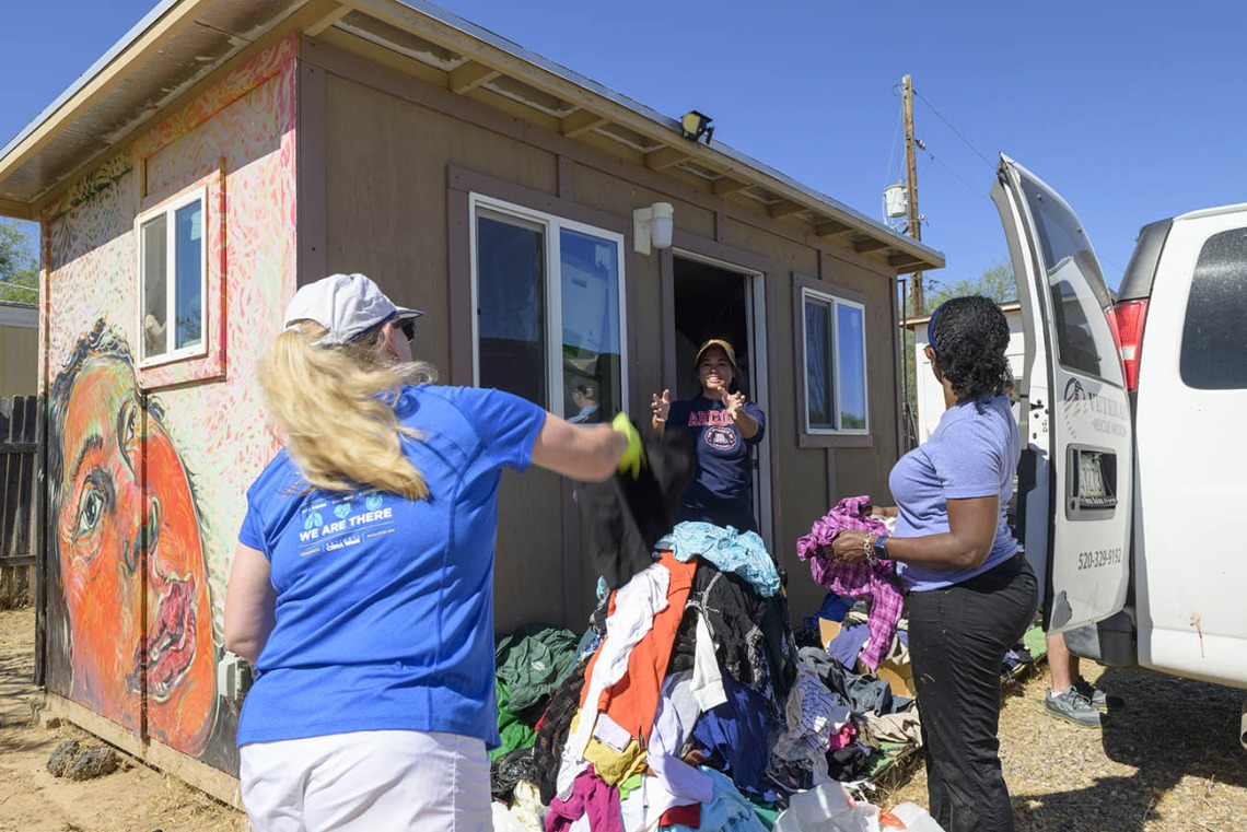 Three women sorting a big pile of donated clothing outside of a small building. 