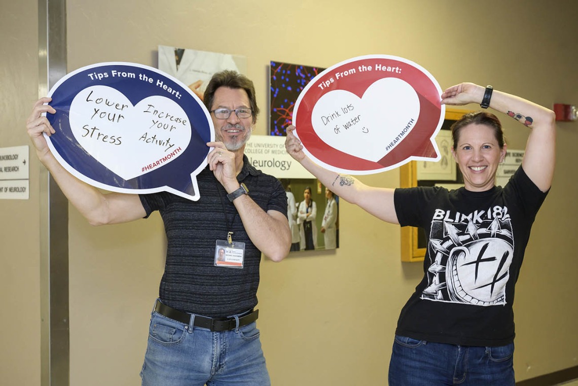 Man and woman in dark shirts hold up heart posters