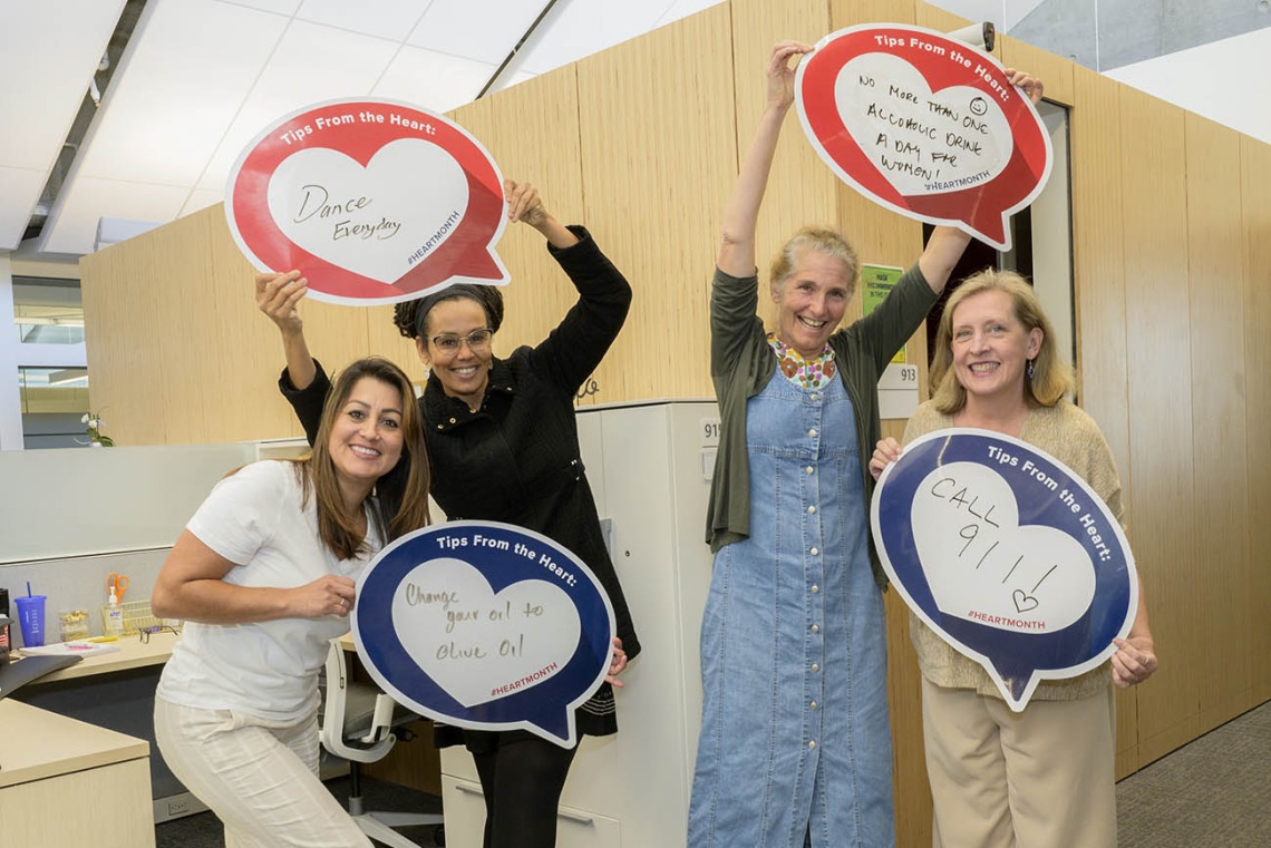 4 woman stand in an office holding heart posters. 