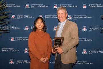 The College of Medicine – Tucson’s Dr. Alice Min stands next to Dr. Gregory L. DeSilva after presenting him with an award, which he is holding. 