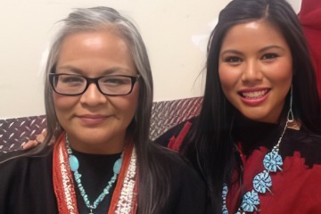 A smiling mother with gray hair stands with her adult daughter.