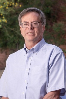 Portrait of a middle-aged white man with glasses smiling. 