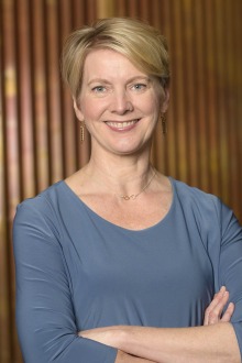 Woman with short blond hair wearing a blue blouse and arms folded