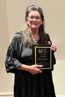 Middle-aged woman with long brown and gray hair holding a plaque. 