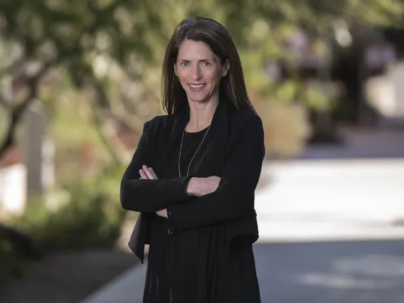 White woman in dark blouse with arms folded in outdoor setting. 