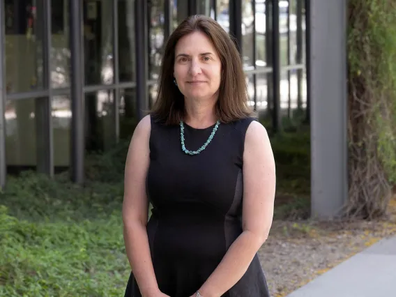 White woman with shoulder-length brown hair wearing a black dress standing outside.