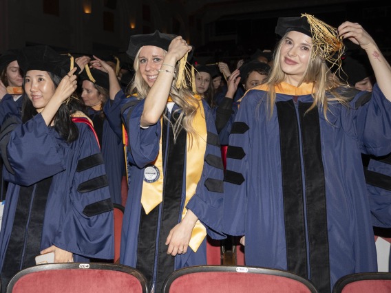 Several nursing graduate in caps and gowns move the tassels on their caps from one side to the other. 