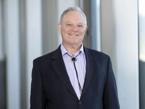 Alt Text: Portrait of Dr. Geoffrey Rubin smiling and wearing a suit coat, collared shirt and bolo tie.