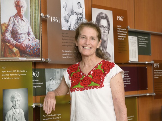Environmental portrait of Dr. Kiser, a middle-aged, light-skinned woman with light brown hear, smiling  in front of portraits on a wall.