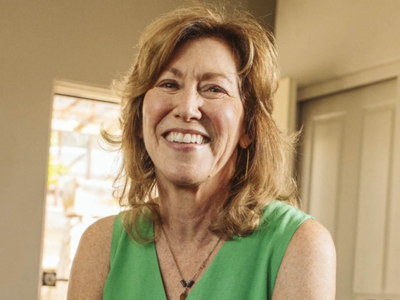 Older woman with shoulder-length brown hair wearing a green top and smiling