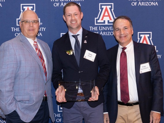 Dr. Chris Goettl holds a glass award and stands next to Dr. Frederic Wondisford, dean of the UArizona College of Medicine – Phoenix, and JP Roczniak, CEO of the UArizona Foundation.