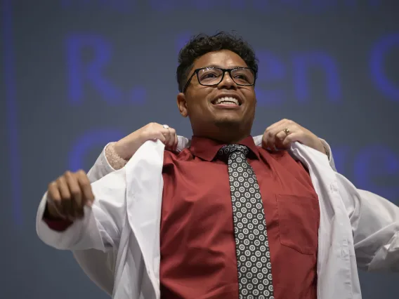 A University of Arizona R. Ken Coit College of Pharmacy student smiles as he puts on his white coat.