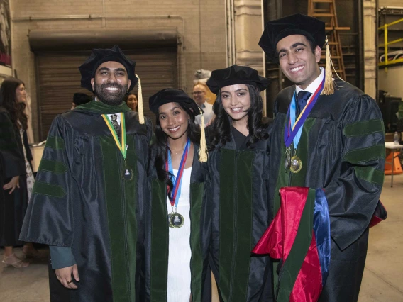 Four University of Arizona College of Medicine – Tucson medical students wearing graduation caps and gowns stand side by side, smiling, before their graduation ceremony. 