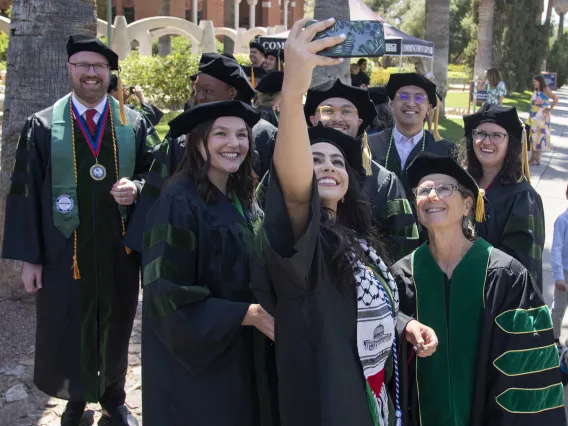 Students from the University of Arizona College of Medicine – Tucson, dressed in graduation caps and gowns, take a selfie outside on their way to the commencement ceremony.