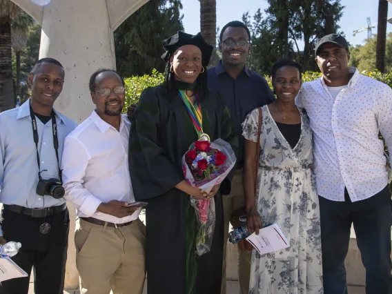 A University of Arizona College of Medicine – Tucson graduate in a cap and gown smiles as she holds flowers while surrounded by family and friends.