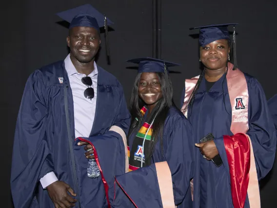 Three University of Arizona Mel and Enid Zuckerman College of Public Health students, all wearing graduation caps and gowns, stand next to each other and smile.