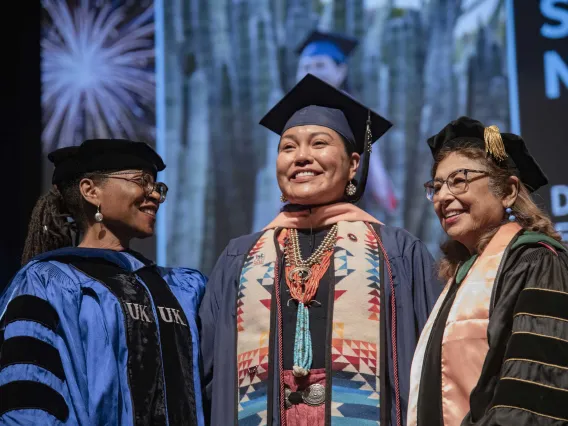 A University of Arizona Mel and Enid Zuckerman College of Public Health student smiles as she stands between two faculty members. All are wearing graduation regalia.