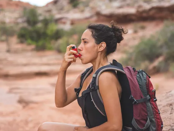 Woman with chronic asthma using inhaler while hiking in the desert