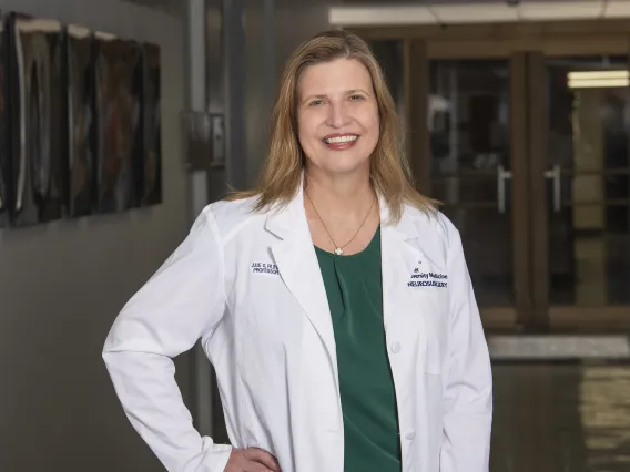 Female doctor wearing a white coat and green blouse stands in a hallway on the College of Medicine – Tucson campus.