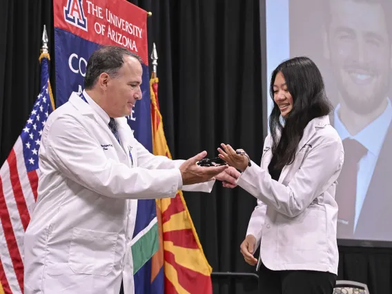 University of Arizona College of Medicine – Phoenix Dean Fred Wondisford presents a stethoscope to a new medical student. Both are wearing white medical coats. 