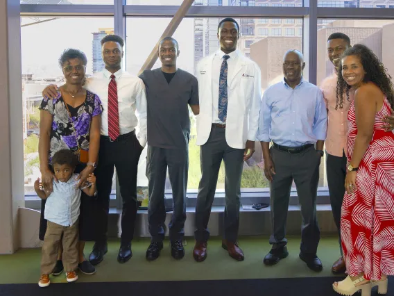 Several family members stand on each side of a University of Arizona College of Medicine – Phoenix student who is wearing a medical white coat. All are smiling.