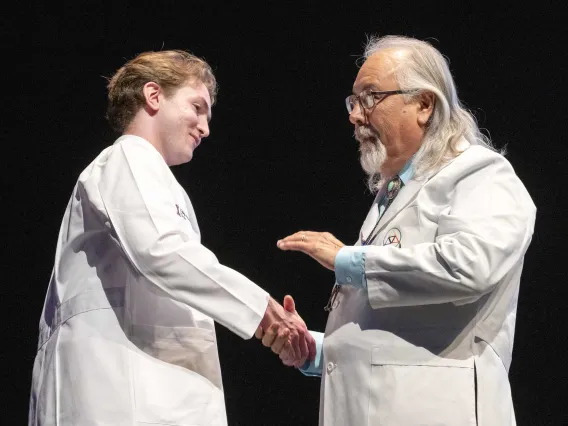 A University of Arizona College of Medicine – Tucson professor shakes hands with a new medical student. Both are wearing medical white coats.