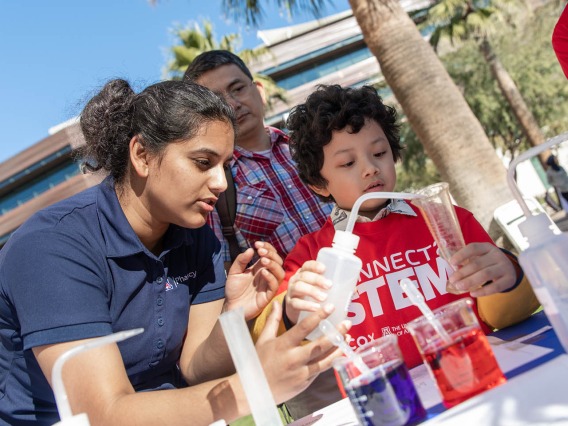 Volunteer with the University of Arizona College of Pharmacy demonstrates chemistry with a young visitor.