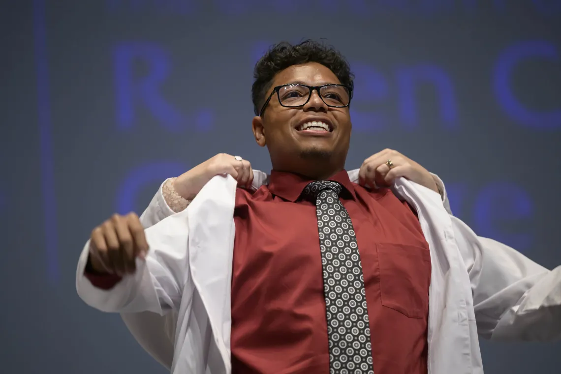 A University of Arizona R. Ken Coit College of Pharmacy student smiles as he puts on his white coat.