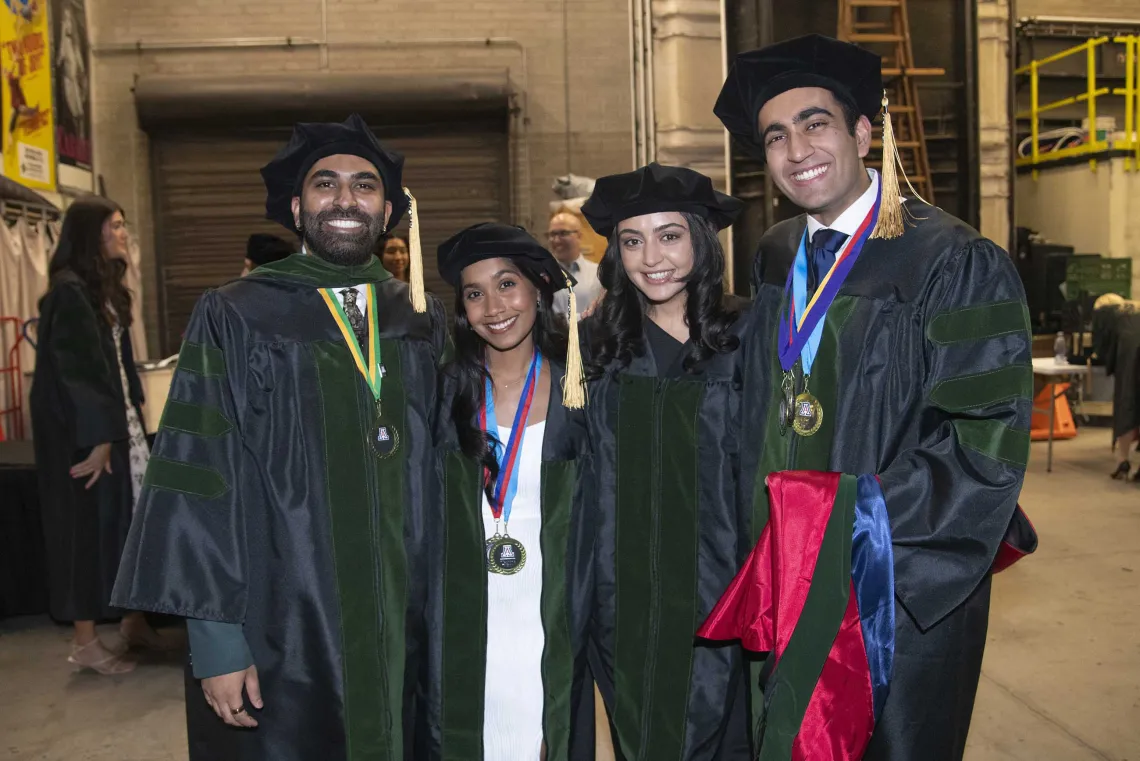 Four University of Arizona College of Medicine – Tucson medical students wearing graduation caps and gowns stand side by side, smiling, before their graduation ceremony. 