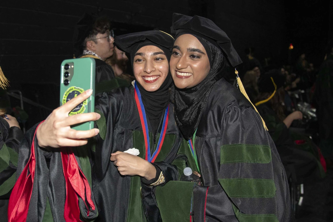 Two University of Arizona College of Medicine – Tucson students in graduation regalia take a selfie before their graduation ceremony.