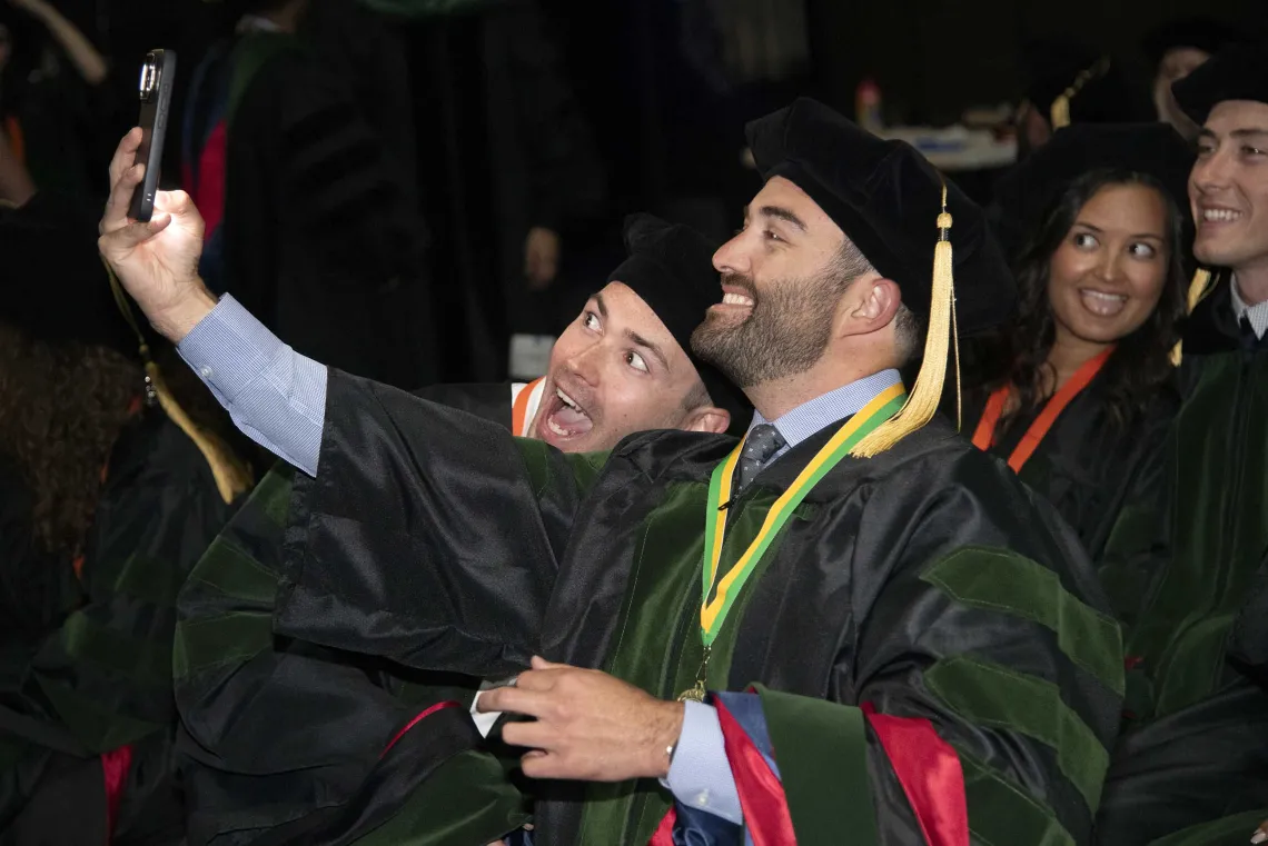 Two University of Arizona College of Medicine – Tucson students in graduation regalia take a selfie before their graduation ceremony. 