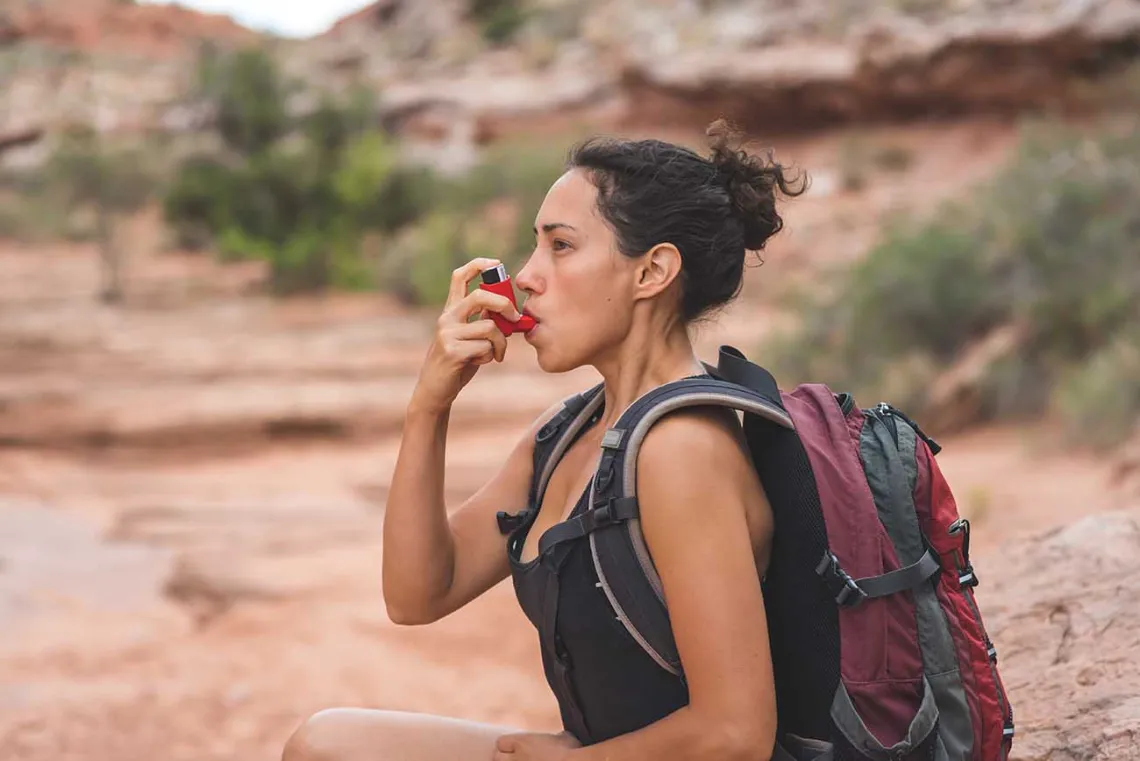 Woman with chronic asthma using inhaler while hiking in the desert