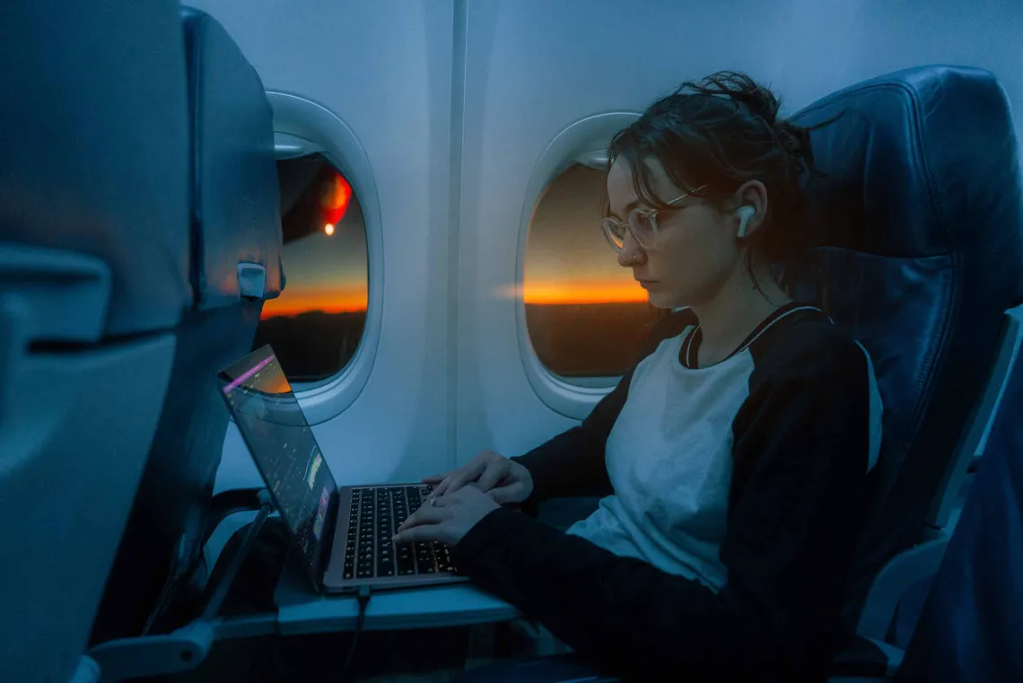 Passenger on plane working on laptop at daybreak 