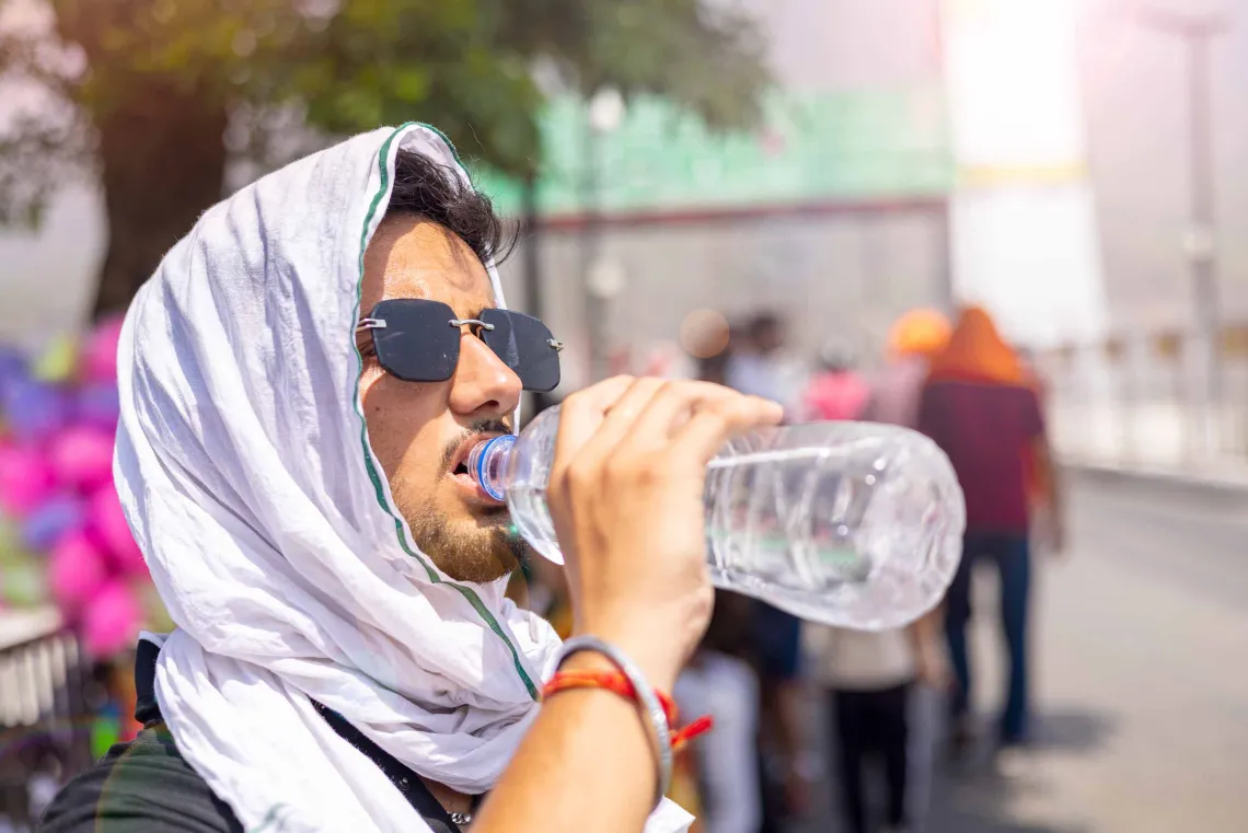 A photo illustration of a man drinking water and covering his head while exposed to extreme heat