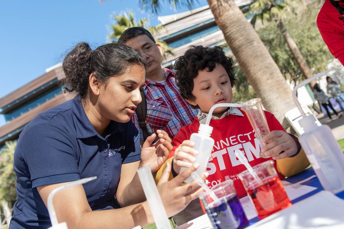 Volunteer with the University of Arizona College of Pharmacy demonstrates chemistry with a young visitor.
