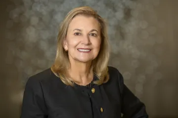 Woman with shoulder-length blonde hair wearing a black suit jacket.