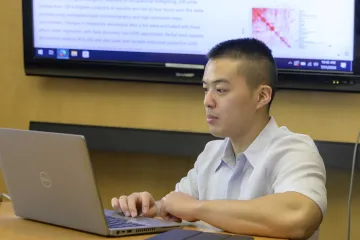 A student reviews data on a laptop in a conference room