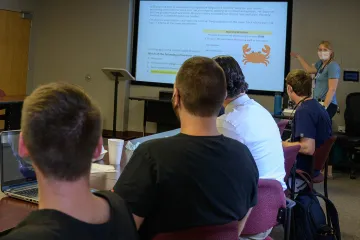 health professions students sit in a classroom while a doctor lectures in front of a projector screen