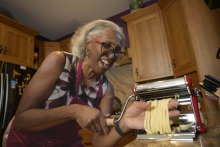 Woman making fresh pasta in her kitchen while smiling joyfully.