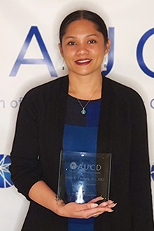 Jacy K. Farkas stands in front of an AUCD backdrop holding the glass award she won. 